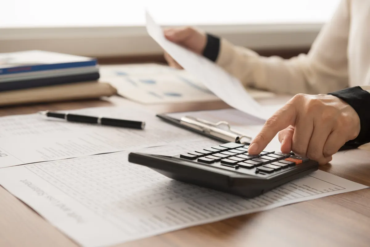 Person working a calculator over financial statements while reviewing a document at a desk