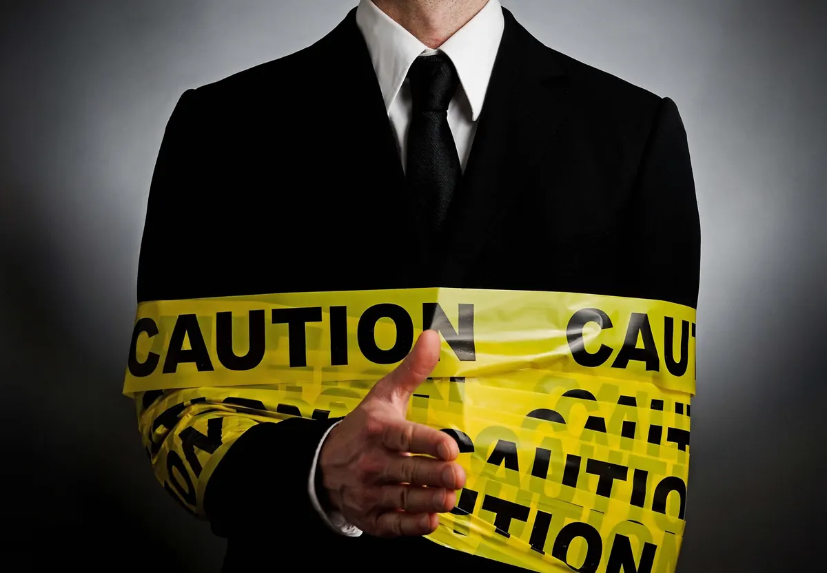 Businessman in a suit offering a handshake while his arm is wrapped in yellow caution tape
