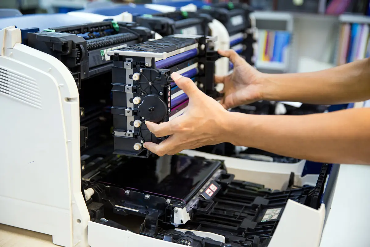 Technician sliding a color drum unit out of an open laser printer