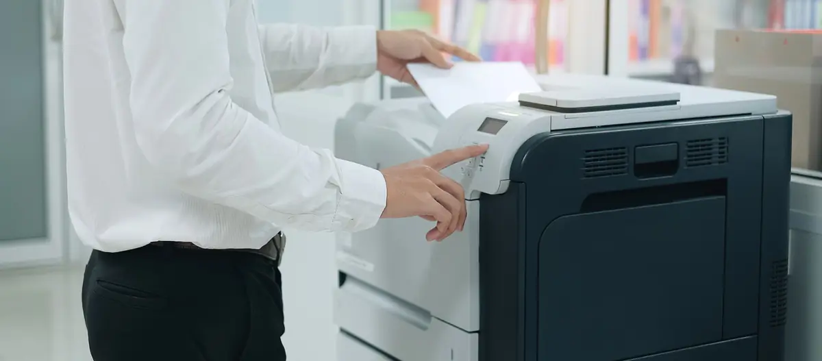 Office worker placing a sheet of paper on a printer and pressing a control button