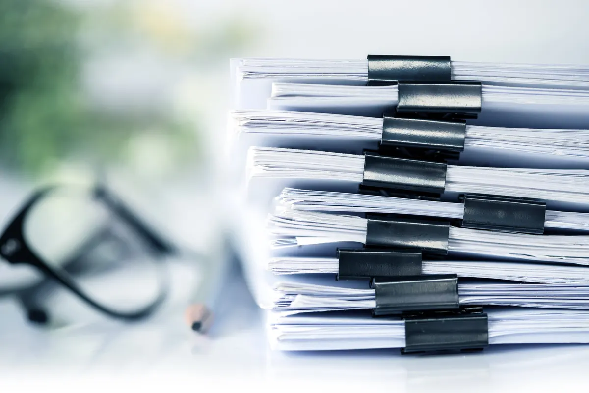 Tall stack of printed documents held together with black binder clips on an office desk