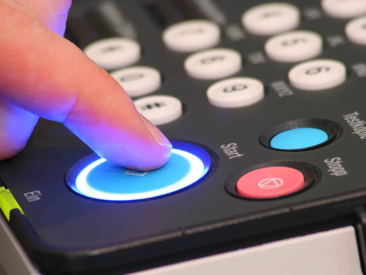 Finger pressing the illuminated start button on a copier control panel, ready to print